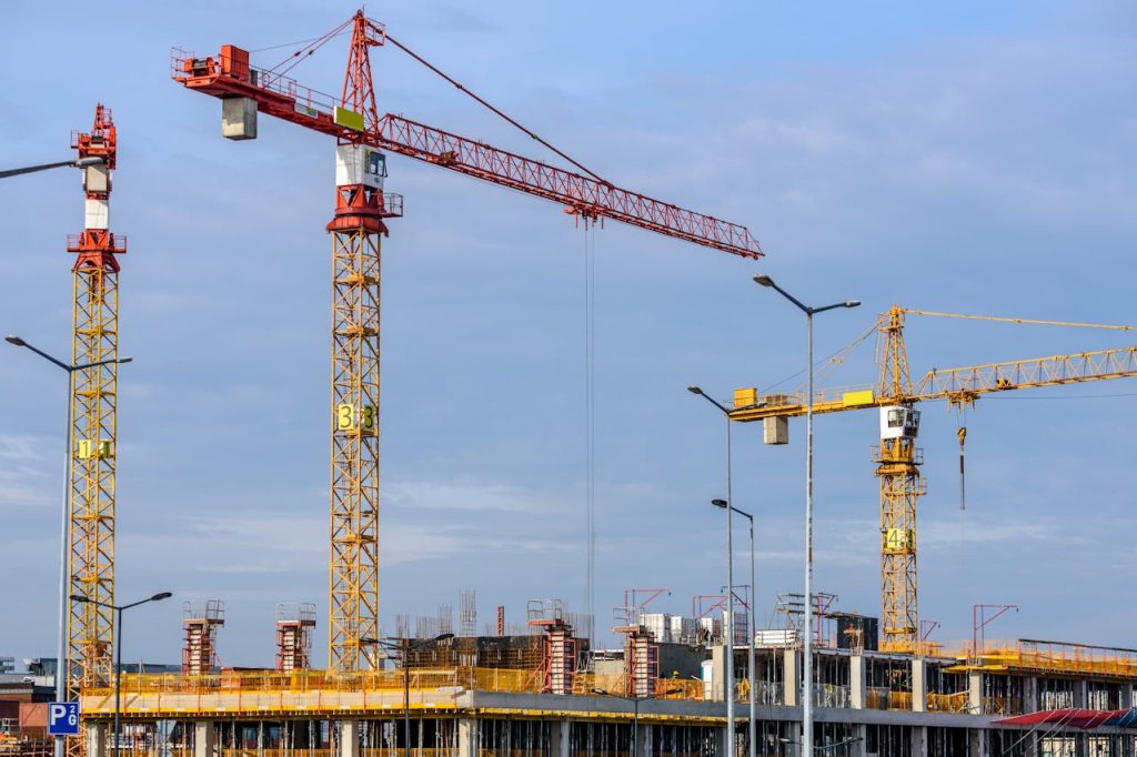 Multiple tower cranes working on a large construction site with blue sky backdrop.