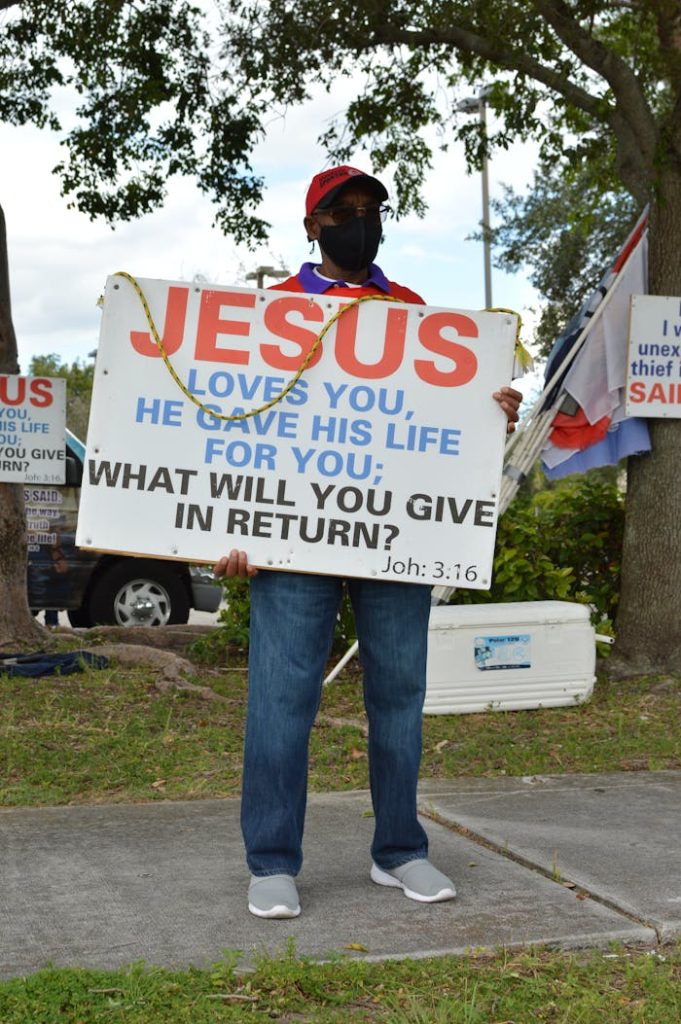 A man holding a Jesus-themed sign outdoors, promoting religious messages.