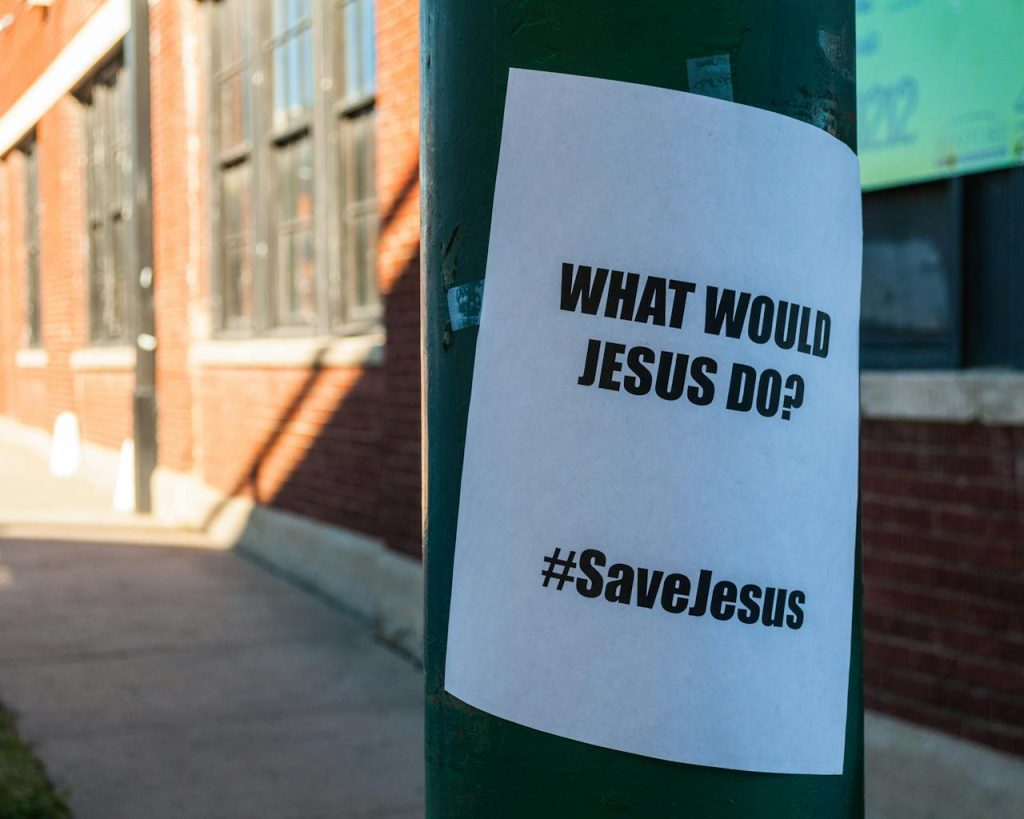 A flyer on a city street pole with the message 'What Would Jesus Do?' and '#SaveJesus'.